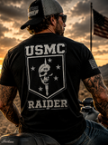 Man wearing a USMC Raider t-shirt with a skull design, sitting on a motorcycle against a sunset sky.