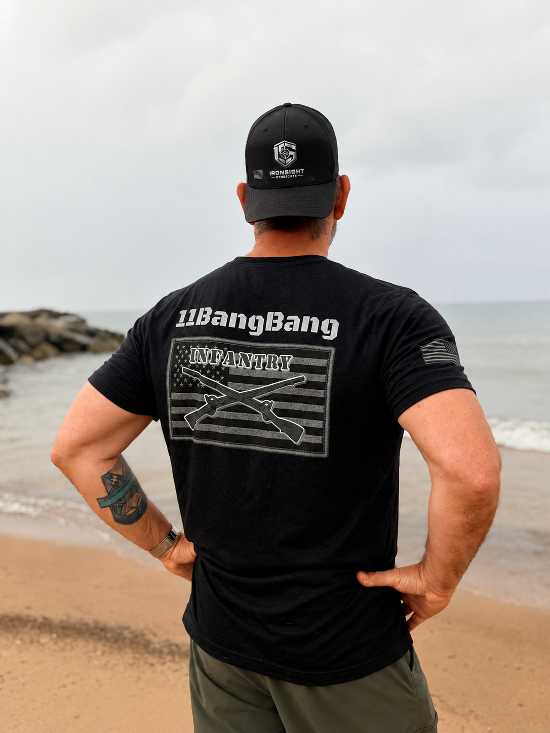 Man wearing an IronSight Syndicate snapback hat and 11BangBang Infantry T-shirt standing on a beach
